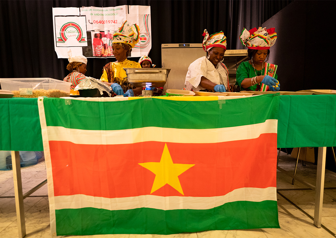 Drie vrouwen die eten bereiden met een Surinaamse vlag op de voorgrond