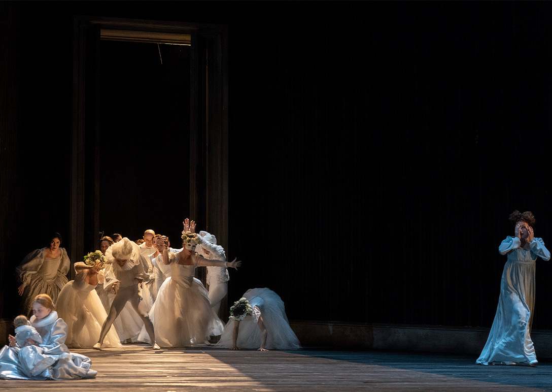 Scene from Maria Stuarda; girl with doll in foreground, ensemble dressed in white in background