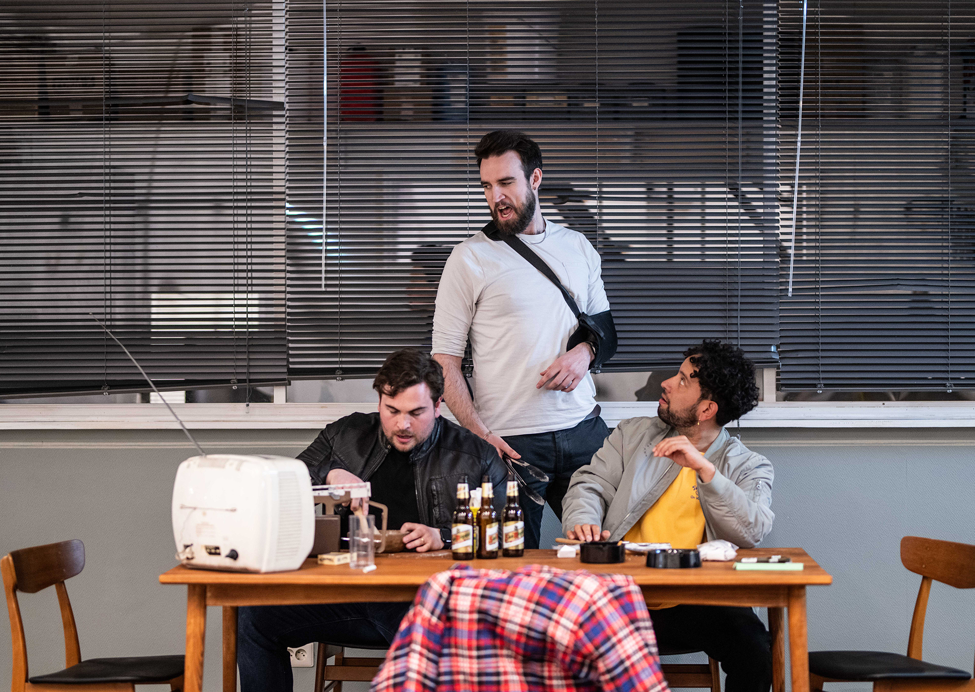 Drie mannen rondom tafel met drank, ruzie makend