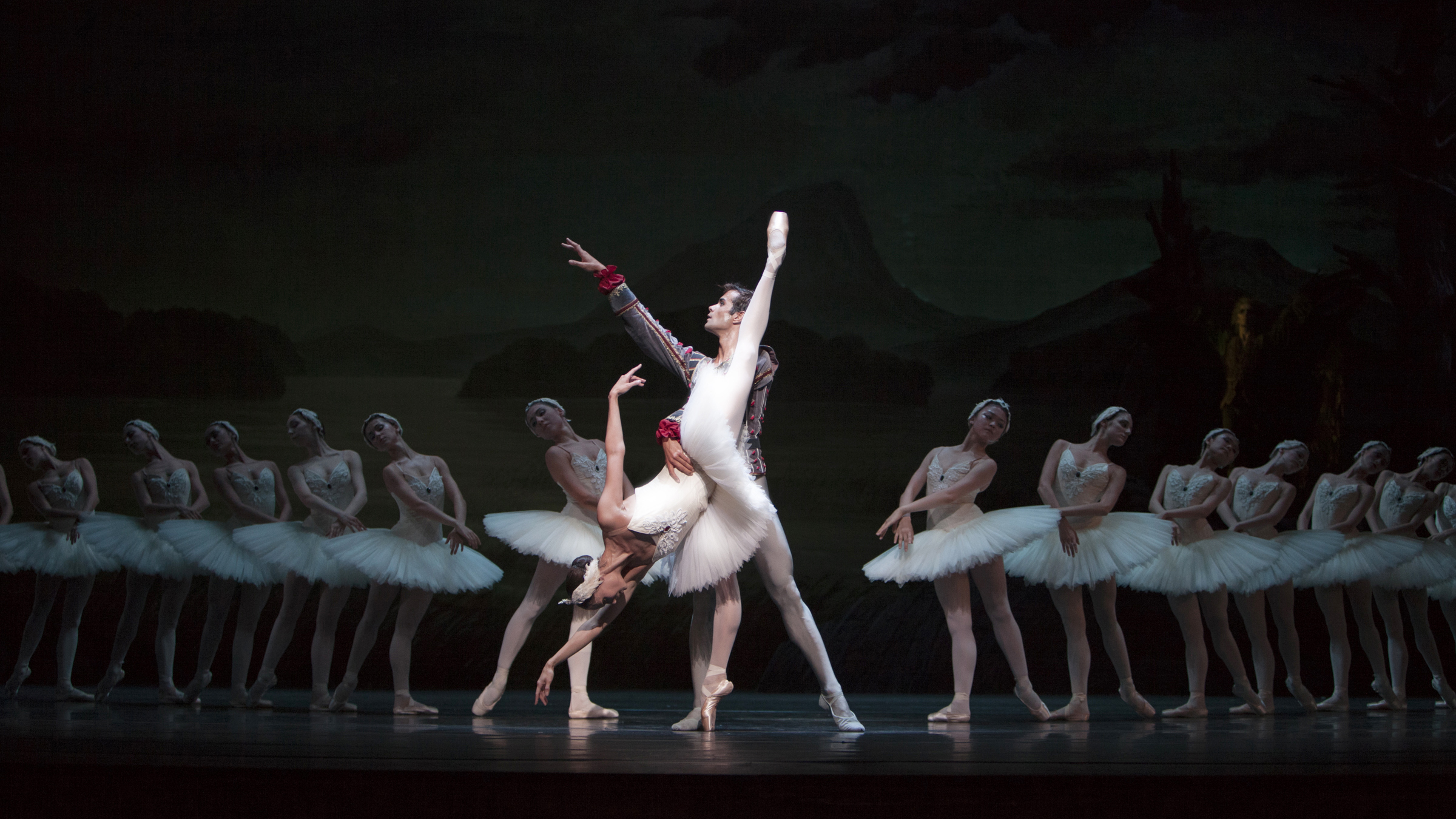 Swan lake, a man and a woman are standing at the center, at the sides in the shadows are more dancers