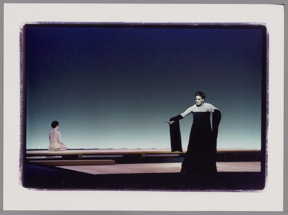 A big woman in geisha clothes in front of the scene and someone  far away in the back in Japanese clothes in pink